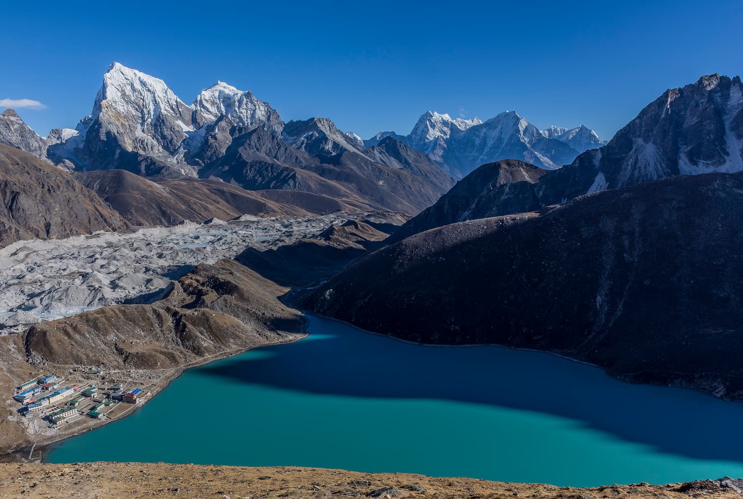 The turquoise Gokyo lake and village beside the grey Ngozumpa Glacier