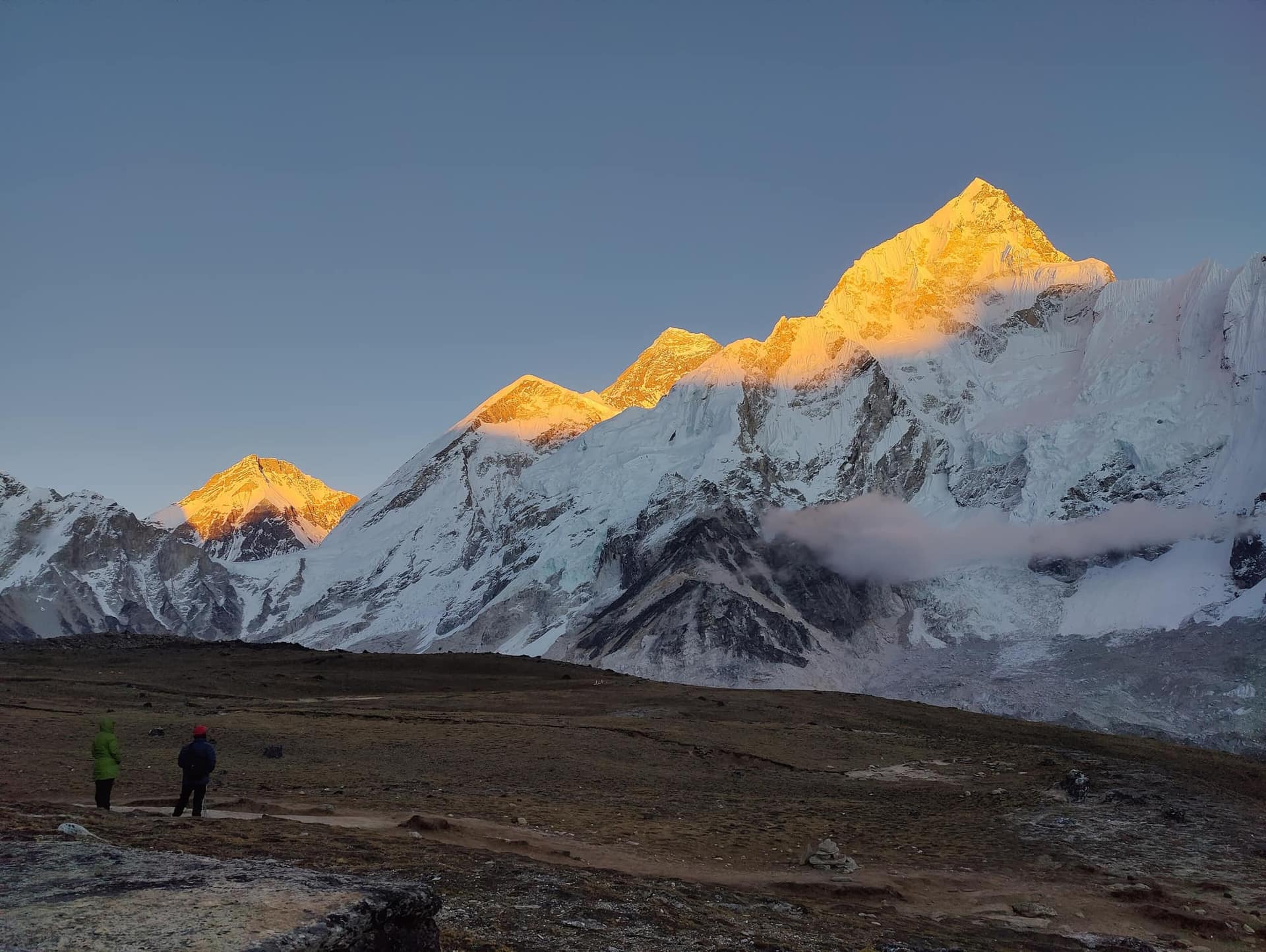Everest and Nuptse catching the last golden light above the Khumbu, with two trekkers in the foreground