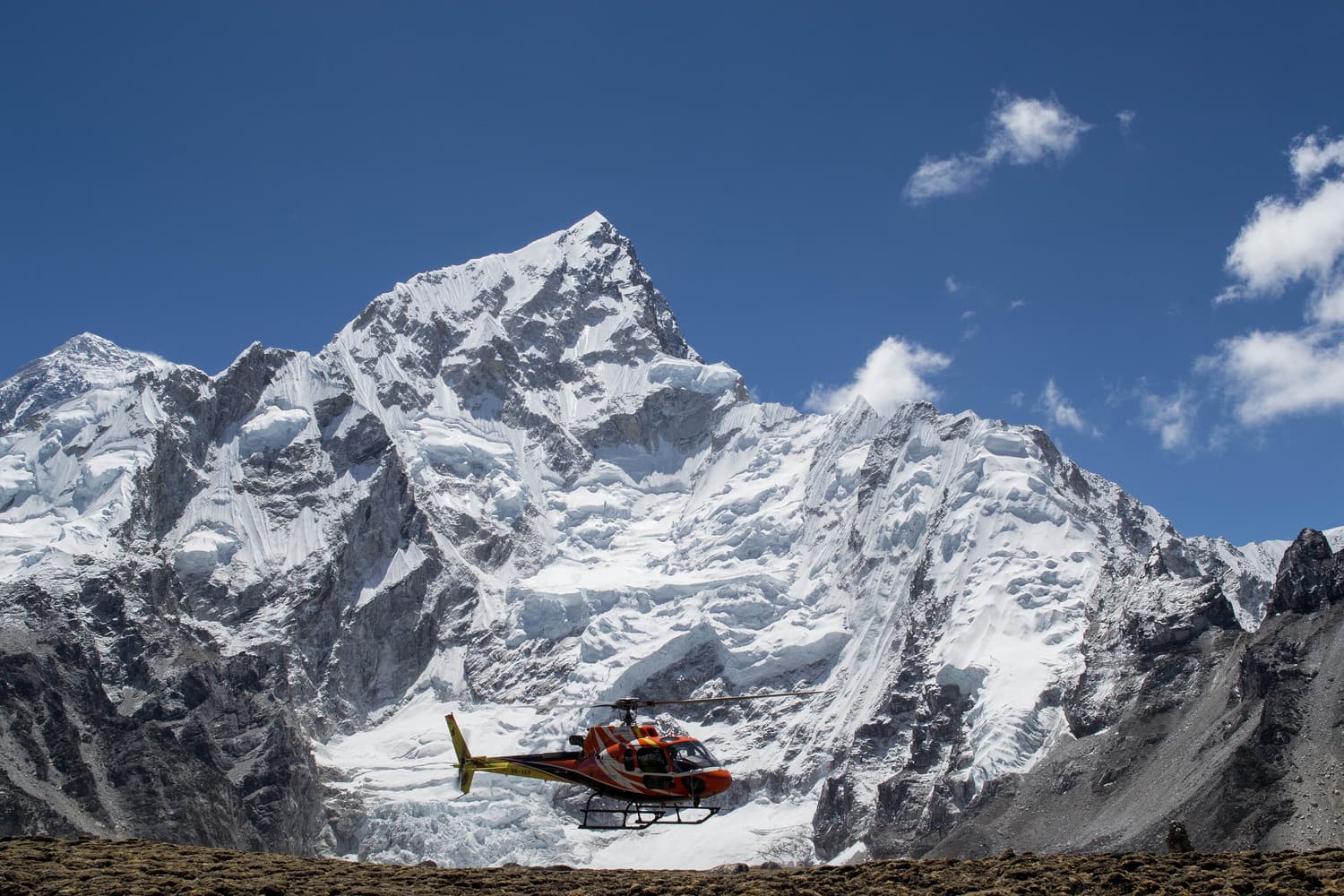 A helicopter lifting off at Everest Base Camp beneath the icy face of Nuptse
